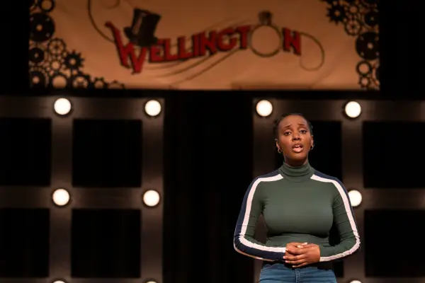 Tameka Griffiths as Bracia, standing on stage, hands clasped, singing