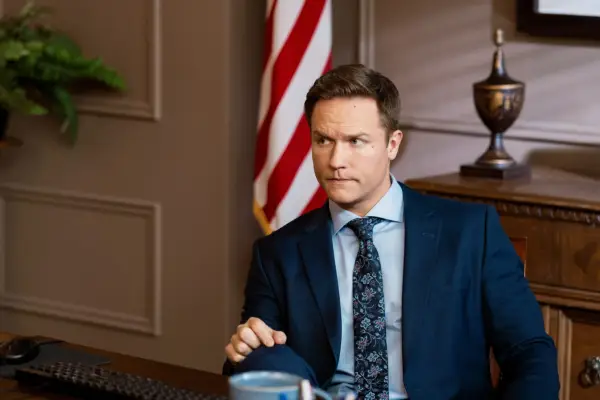 Scott Porter as Mayor Paul Randolph, sat behind a desk in an office, wearing a suit, the US flag in the background