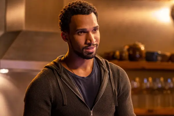Nathan Mitchell as Zion, stood in his kitchen, smiling, wearing a dark-coloured hoodie