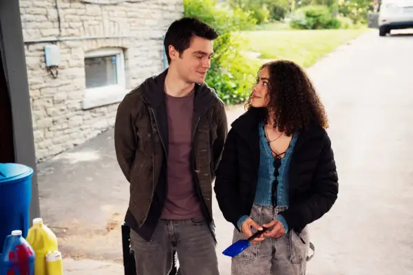 Felix Mallard as Marcus Baker and Antonia Gentry as Ginny, stood next to one another in a garage, looking at one another