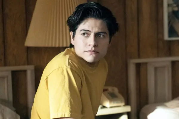 Uber wearing a yellow t-shirt, sat on the edge of the bed, looking to his left