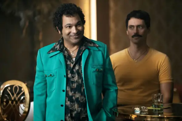 Papo wearing a turquoise jacket, walking into a room, smiling