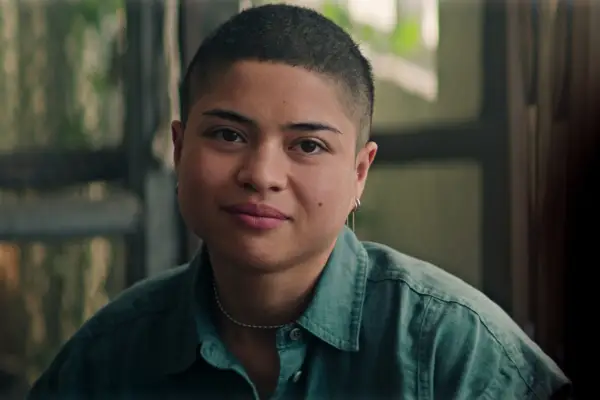 b as Phoenix in You season 5 smiling as they sit by a window in a shirt.