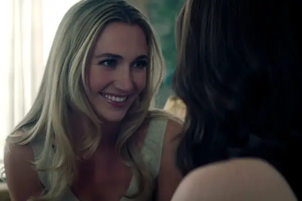 Tilly Keeper as Lady Phoebe in You season 5 smiling as she embraces Kate on a sofa in a hotel room.