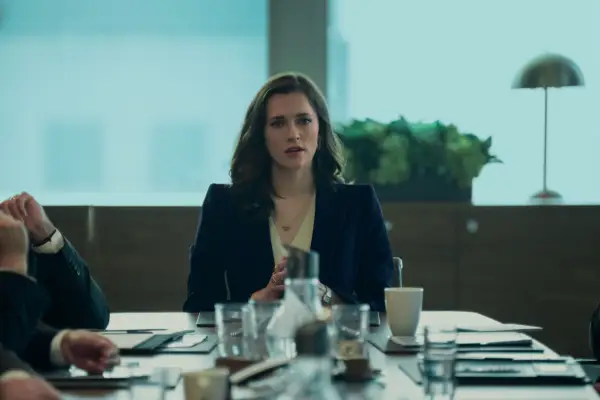 Charlotte Ritchie as Kate Lockwood in You sitting at the head of a boardroom table, wearing a blue blazer and looking seriously across the room.