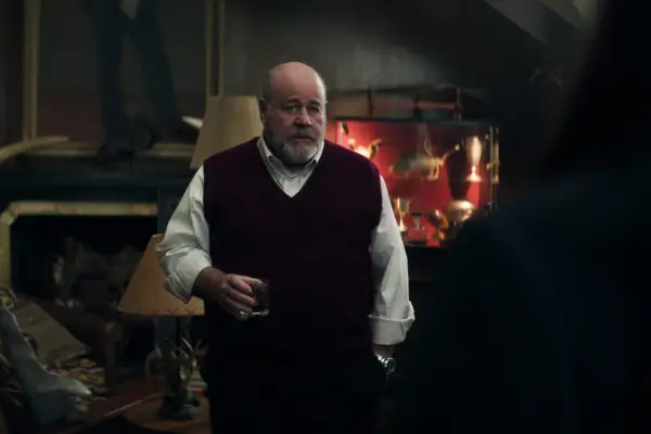 Michael Dempsey as Buffalo Bob Cain in You season 5 holding a glass of whiskey as he stands in his living room with a hand in his pocket.