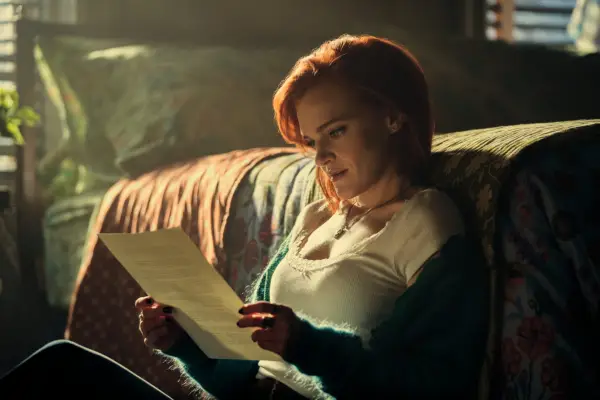Madeline Brewer as Bronte in You, reading a piece of paper while sat on the floor of her bedroom.
