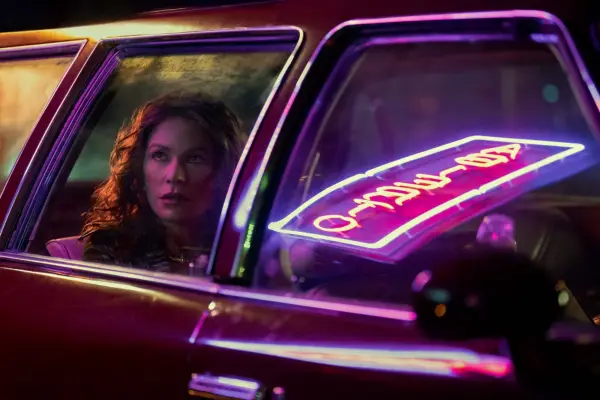 Griselda Blanco (played by Sofia Vergara) sits in a car, with a neon sign reflected in the passenger window