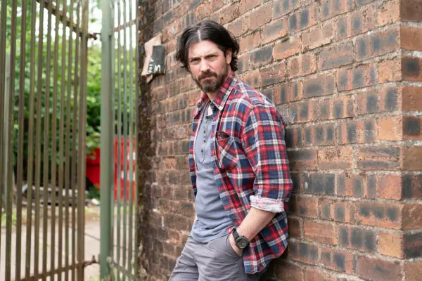 Cammy standing with his back against a wall, looking directly at the camera