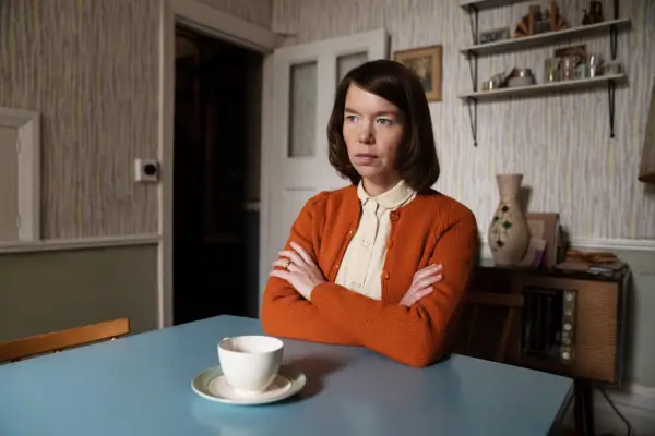 Lily sat at a kitchen table with her arms crossed and a cup and saucer placed before her