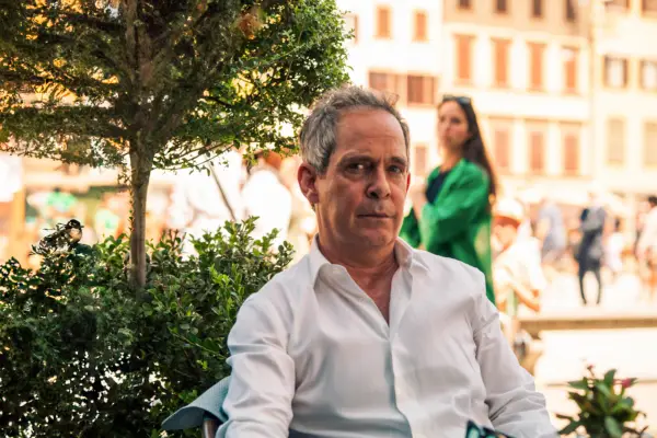 Tom Hollander in The Iris Affair, sat outside and wearing a shirt.