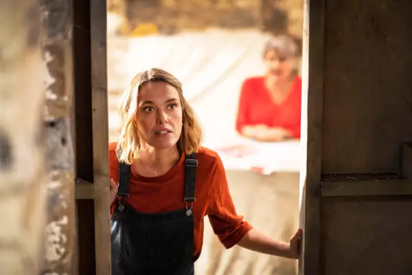 Martha standing in a doorway looking into a building with a surprised expression on her face