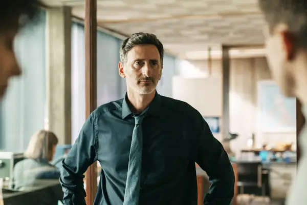 Andy Gathergood plays Paul Rabbit in Professor T, wearing a suit and tie, standing in an office at the police station