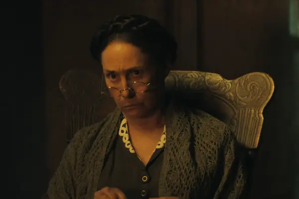 Laurie Metcalf as Augusta Gein in Monster: The Ed Gein Story staring up across her glasses, looking displeased.