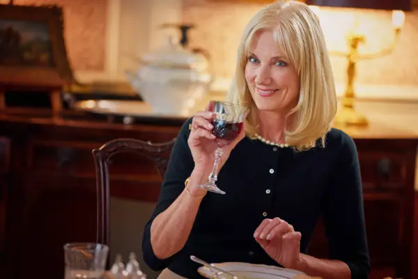 Helen sat at a dining table, drinking red wine and smiling