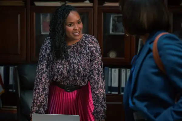 Brittany L Smith as Peggy, leaning on her desk in the mayor