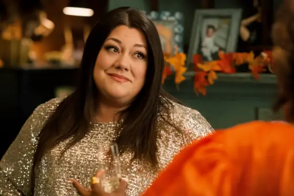 Brooke Elliott as Dana Sue wearing a gold sparkly top, sat on a chair talking to Helen