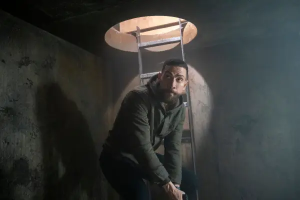 Zeeko Zaki as Special Agent Omar Adom ‘OA’ Zidan standing in a dark underground tunnel and holding his gun downwards, ready to use.