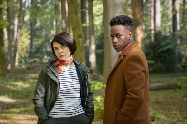 Hannah Donaldson and Romario Simpson star in Granite Harbour standing together in the woods looking into camera
