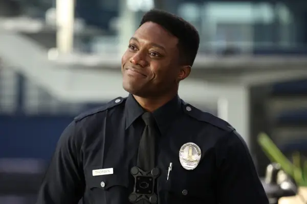 Tru Valentino as Aaron Thorsen in The Rookie standing in his police uniform and smiling.