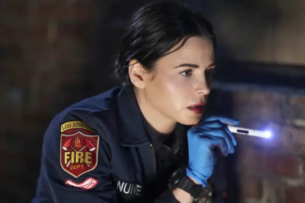 Jenna Dewan as Bailey Nune in The Rookie wearing her firefighter uniform and shining a mini torch into a dark space.