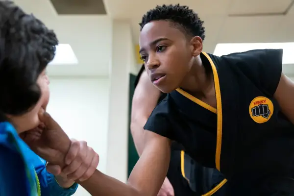 Dallas Dupree Young as Kenny in Cobra Kai wearing a black and orange outfit