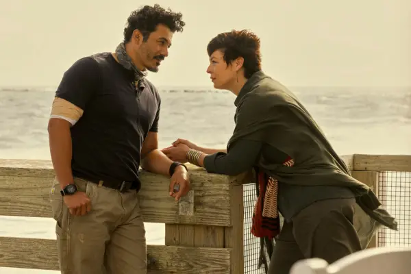 Rigo Sanchez as Lightner and Pollyanna McIntosh as Dalia in Outer Banks having a conversation overlooking the sea and leaning in close to each other.