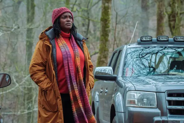 Wunmi Mosaku as DC Riya Ajunwa standing with her hands in her coat pocket standing next to her car and looking ahead in Passenger.