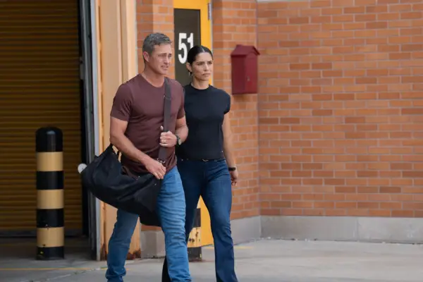 Taylor Kinney as Lieutenant Kelly Severide, Miranda Rae Mayo as Lieutenant Stella Kidd in Chicago Fire season 14 walking out of the building together, with their arms entwined.