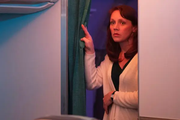 Dr Kate Ward on thew plane, standing in the aisle with her hand on a curtain.