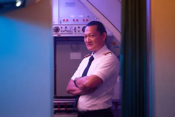 Thomas Chaanhing as Chén, stood up in the plane, with her arms crossed