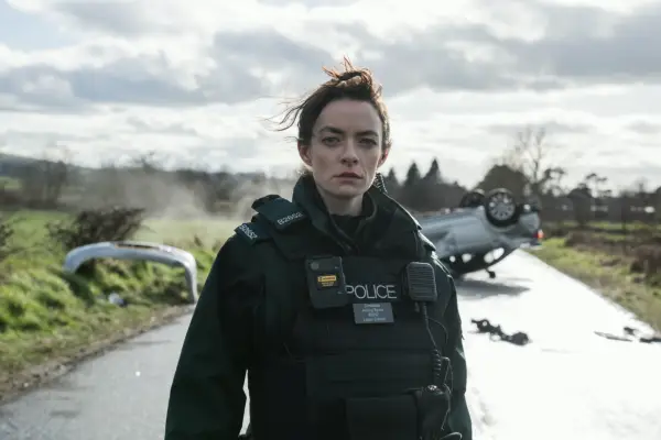 Dearbháile McKinney as Aisling in Blue Lights standing in front of a wrecked car on a road, wearing a police uniform and looking scared.
