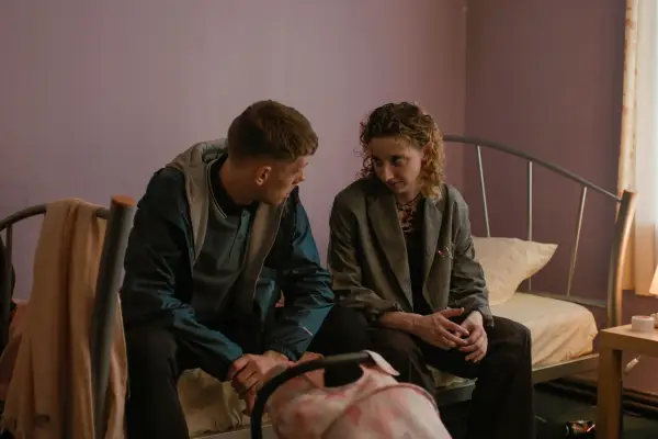 Marco and Casey sit on a bed, with his baby