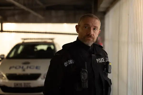 Chris Carson (Martin Freeman) wears police uniform in a car park, with a police vehicle parked in the background