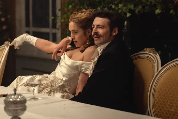 Danielle Galligan and Anthony Boyle star in House of Guinness; they are in character, wearing formal dress at a dinner table, leaning on each other in a fond manner