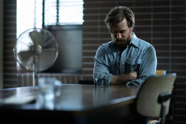 Seth Numrich as Robin Lafferty, sat at a table with his head down in Under the Banner of Heaven