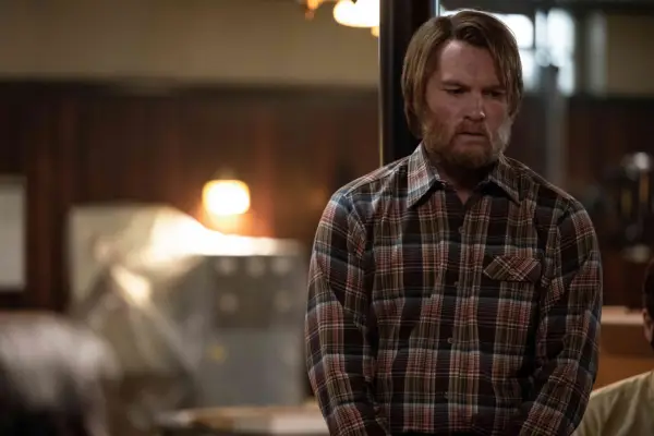 Sam Worthington as Ron Lafferty, with a big beard and wearing a checkered shirt in Under the Banner of Heaven