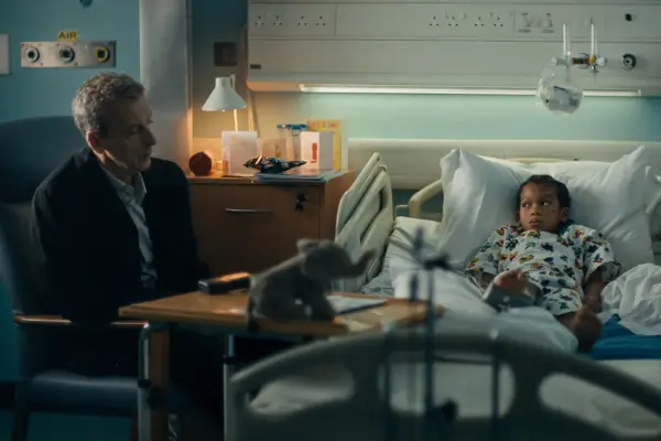 Peter Capaldi sat by a hospital bed that Kaylen Luke is lying on in Criminal Record