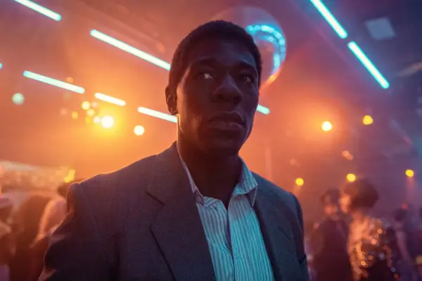 McKinley Belcher III as Detective Ledroit in Eric standing in the middle of a dimly lit nightclub, surrounded by neon lights.