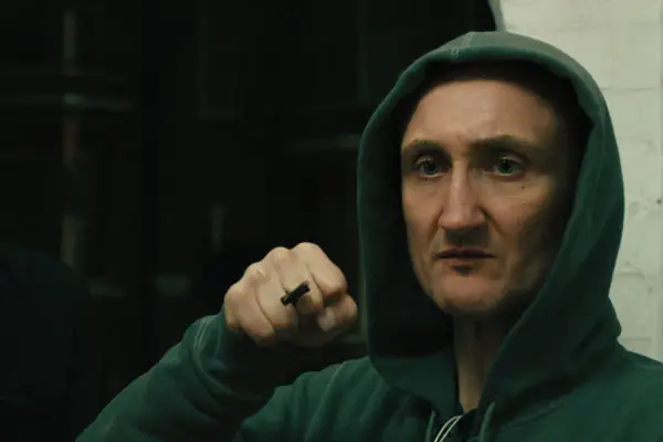 Tom Brooke in Slow Horses, wearing a hood and with his fist raised.