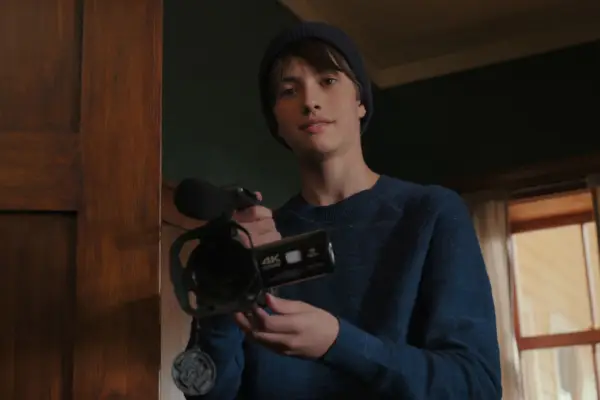 Dean Petriw as Jordan Walter. He is wearing a dark blue jumper and holding a camera, with a slight smile.