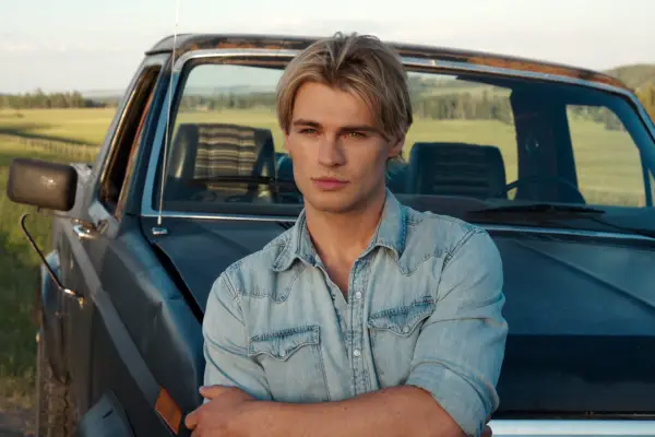 Noah LaLonde as Cole wearing a light blue denim shirt, looking ahead with his arms folded.