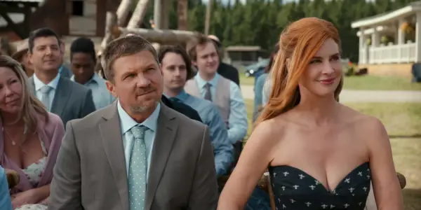 Marc Blucas as George and Sarah Rafferty as Katherine sat down next to each other a wedding, smiling ahead.