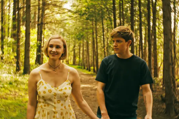 Sarah Gadon as Laura Redman and Mae Martin as Alex Dempsey walking along a forest path holding hands. Laura, who