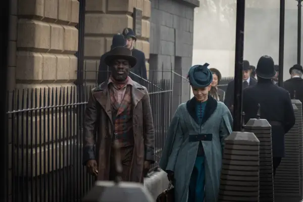 Ansu Kabia as Moses Valentine and Kate Phillips as Eliza Scarlet, walking down a street side by side.