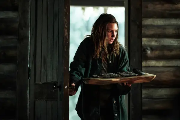 Shauna carrying a tray of rations through the door of the cabin