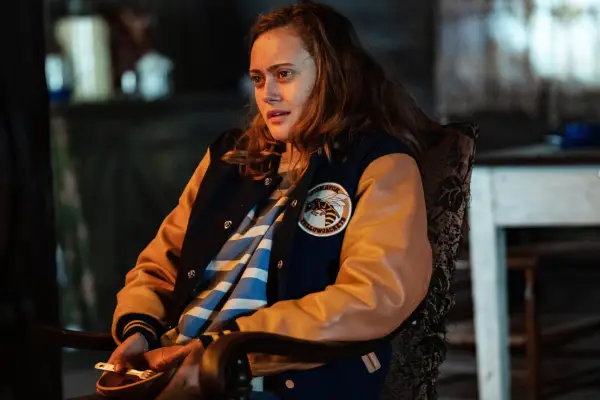 Teen Nat stansing in front of a brick wall holding a bottle of alcohol concealed in a paper bag