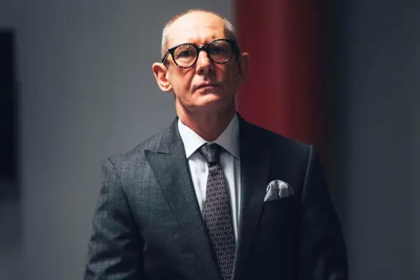 Ian Hart as Bob Rutherford, wearing glasses and a suit
