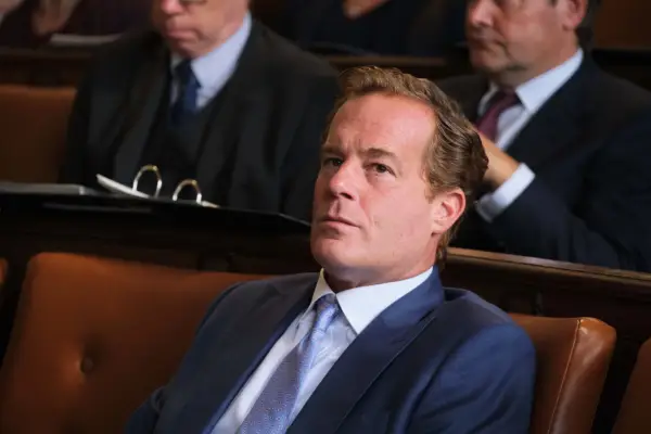 Adam James as Patrick Green QC, wearing a suit, sat down in court