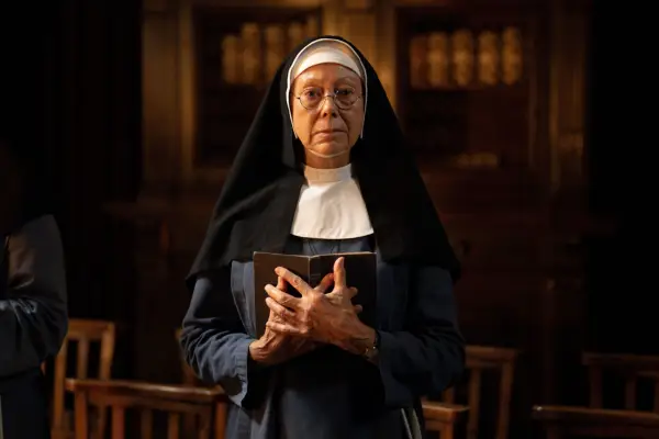 Jenny Agutter as Sister Julienne in Call the Midwife holding a bible to her as she stands in a dimly lit room.